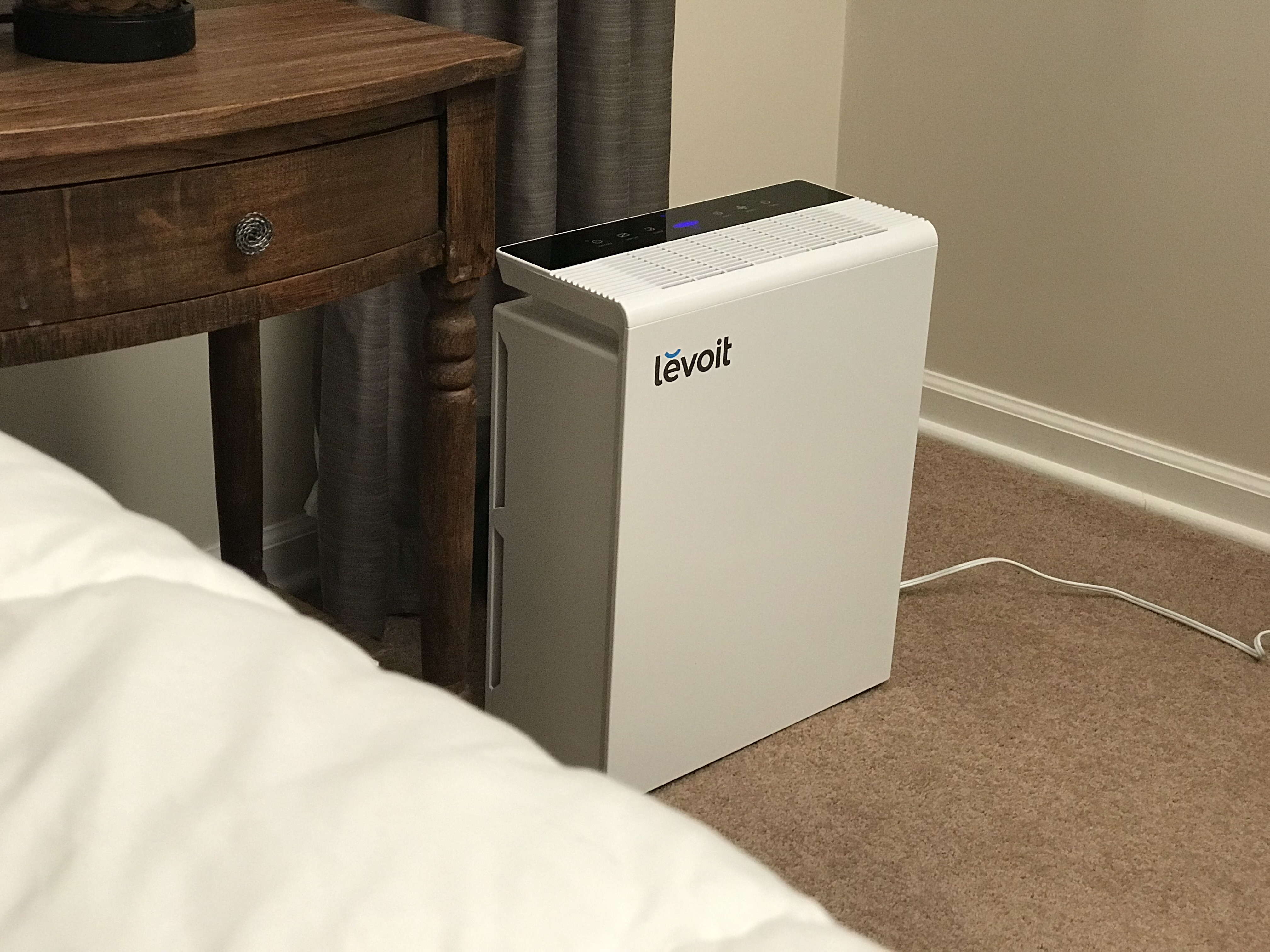 Image of an air purifier by a bed. 